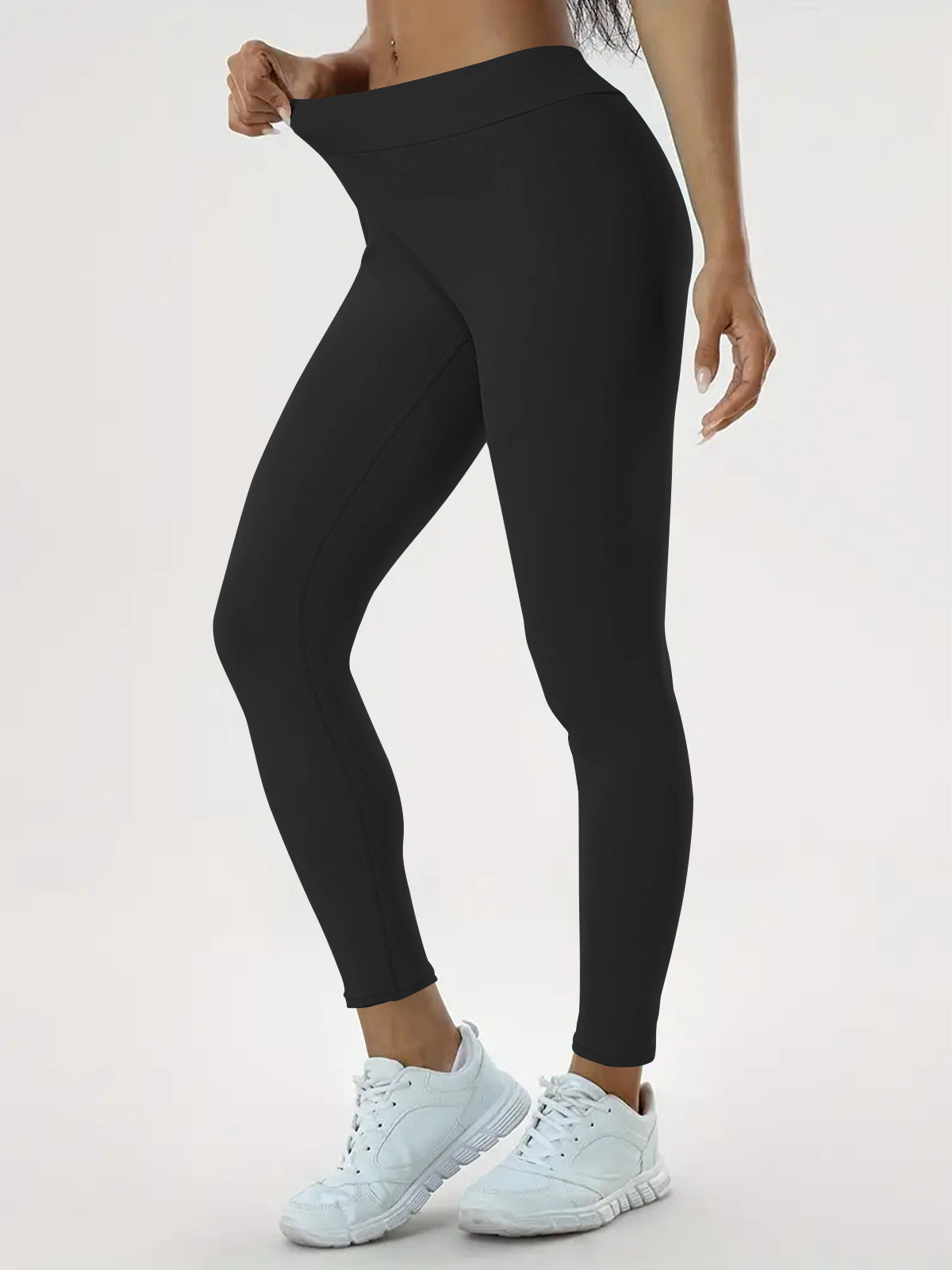 "Person wearing black leggings and white athletic shoes, showing the fit and stretchiness by holding the waistband. Perfect for yoga, fitness, and casual wear."