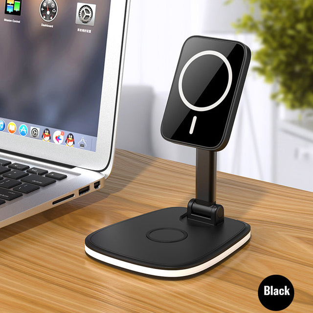 "A black magnetic phone stand is placed on a wooden desk next to a laptop. The stand has a circular magnetic pad for holding a phone and an adjustable arm. The laptop screen shows various icons, including Mission Control, Dashboard, and other applications. The word 'Black' is displayed in the bottom right corner of the image."