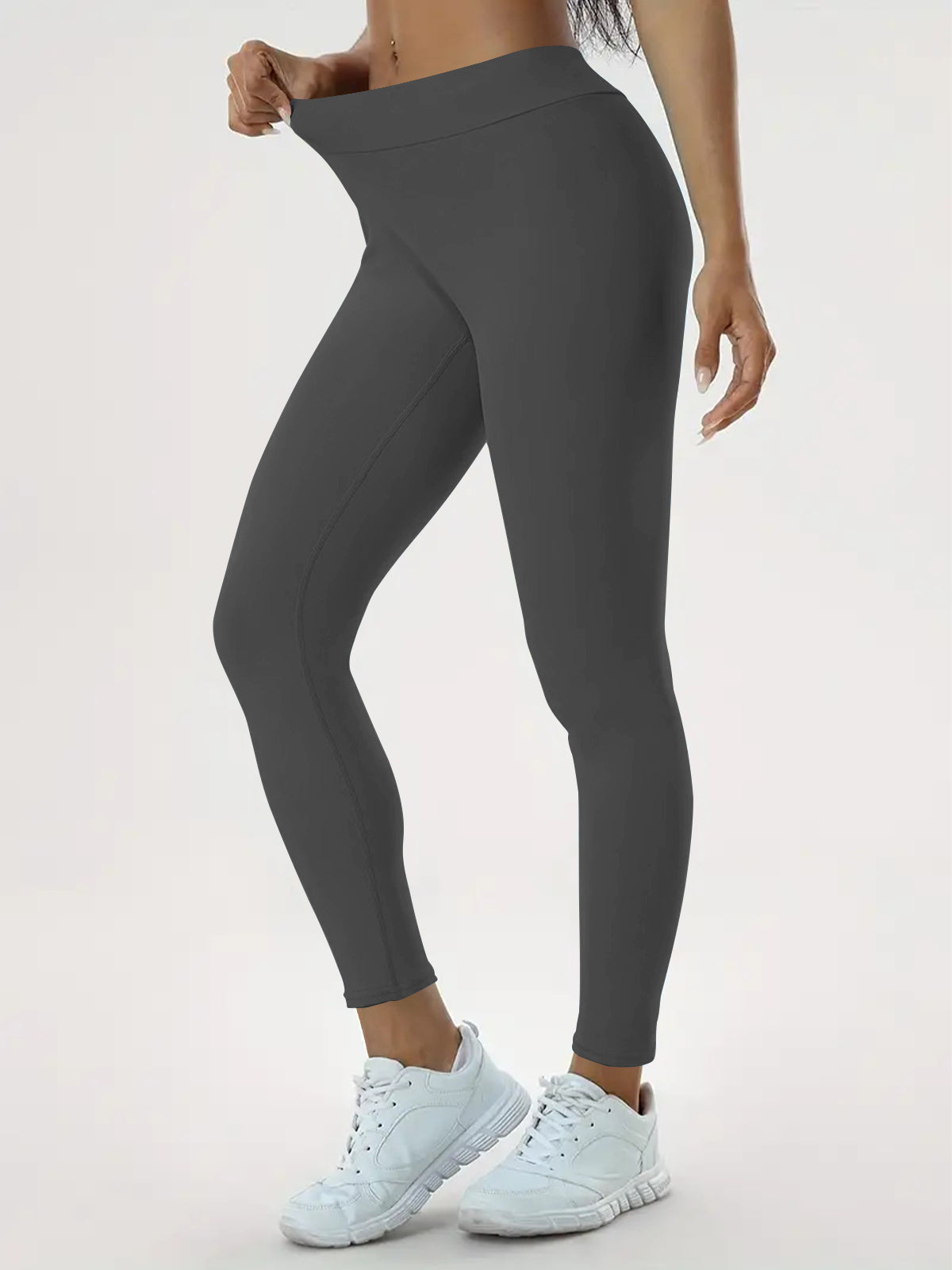 High-waisted stretchy yoga leggings for women in dark gray, showcasing a comfortable fit and flexibility, paired with white sneakers.