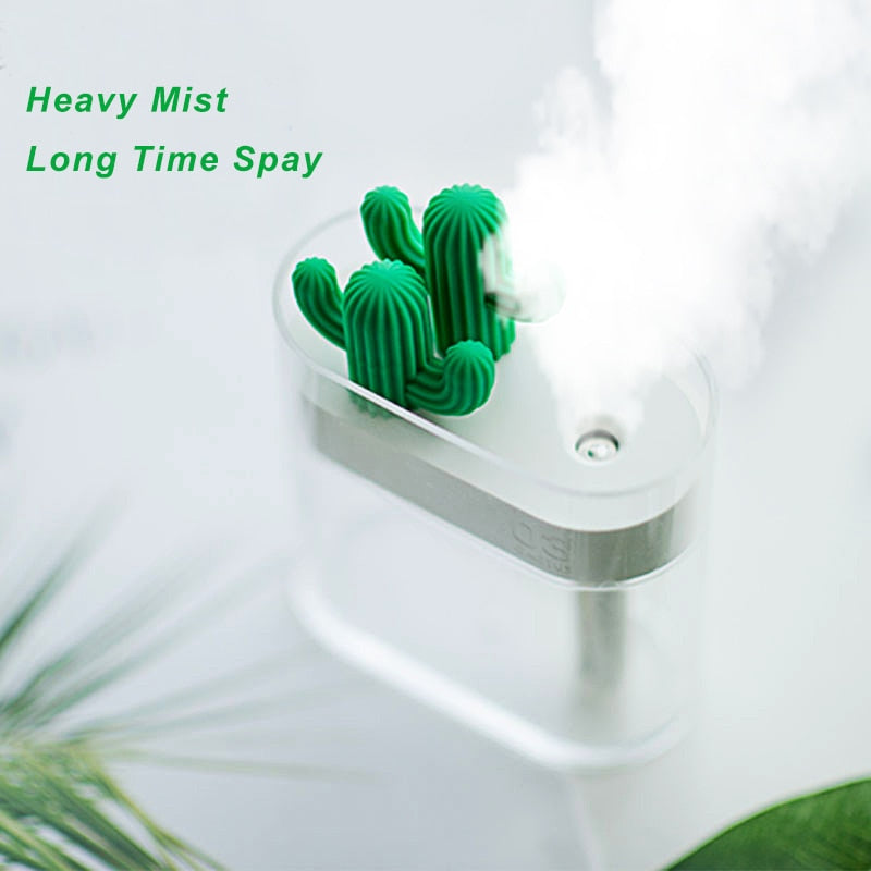 "A small humidifier with a cactus-shaped design is emitting a heavy mist. The text 'Heavy Mist Long Time Spray' is written in green on the left side of the image."