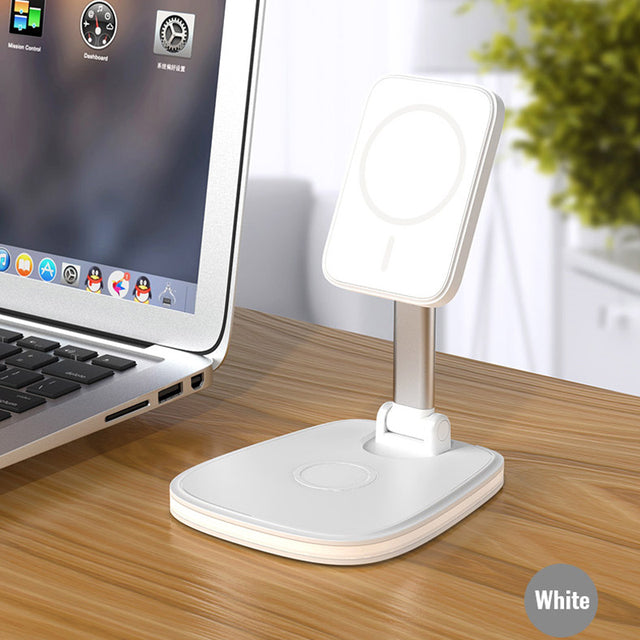 "A white wireless charging stand is placed on a wooden desk next to a laptop. The laptop screen displays various application icons, including Mission Control and Dashboard. The charging stand features a circular charging pad on its base and an adjustable arm holding another circular pad, likely for charging devices such as smartphones or smartwatches. The setup highlights a modern and organized workspace with convenient charging solutions."