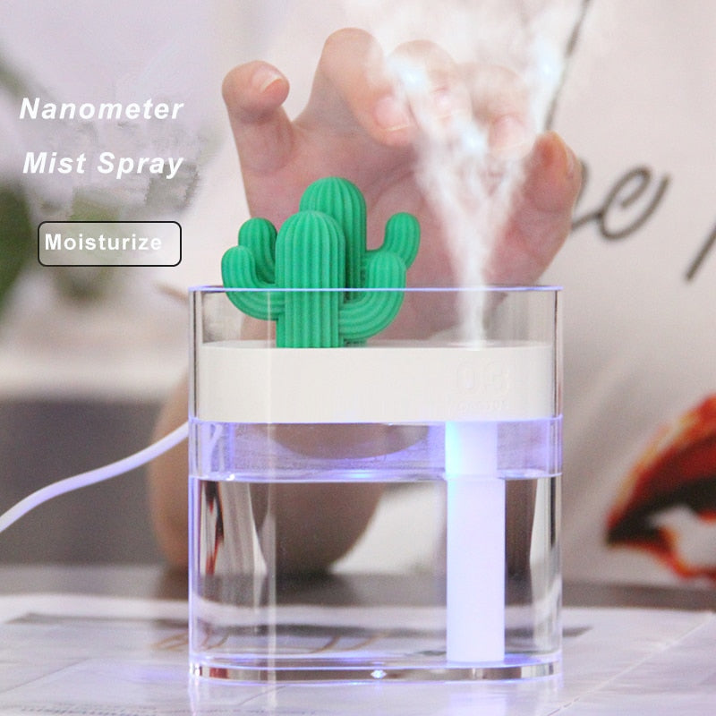 A close-up image of a nanometer mist spray humidifier with a green cactus-shaped top. The device is emitting a fine mist, and a person's hand is visible in the background. The text 'Nanometer Mist Spray' and 'Moisturize' is displayed on the left side of the image. The humidifier is transparent, showing water inside, and is connected to a power source via a white cable."